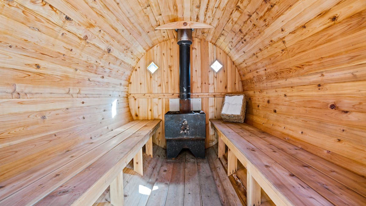 Wooden barrel sauna interior with traditional wood-burning stove and natural cedar benches